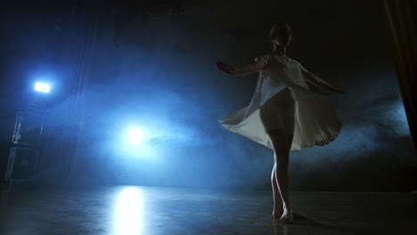 Una-Mujer-De-Danza-Moderna-Con-Un-Vestido-Blanco-Baila-Un-Ballet-Moderno-Salta-Y-Hace-Rotación-En-El-Escenario-Con-Humo-En-Los-Focos-Azules
